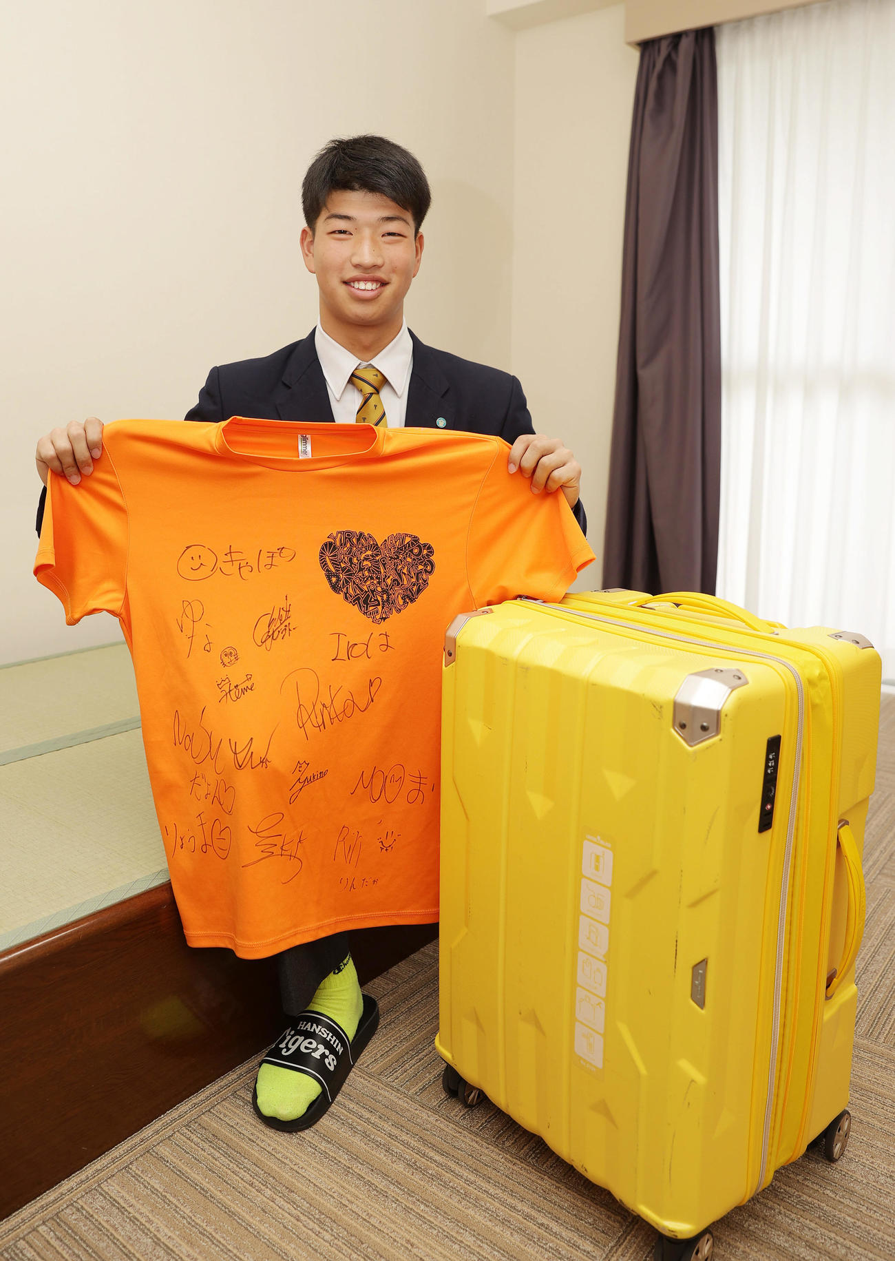 入寮し持ち込んだクラスメートのサインが書かれたTシャツを手に笑顔を見せる阪神ドラフト4位の百崎（撮影・前田充）