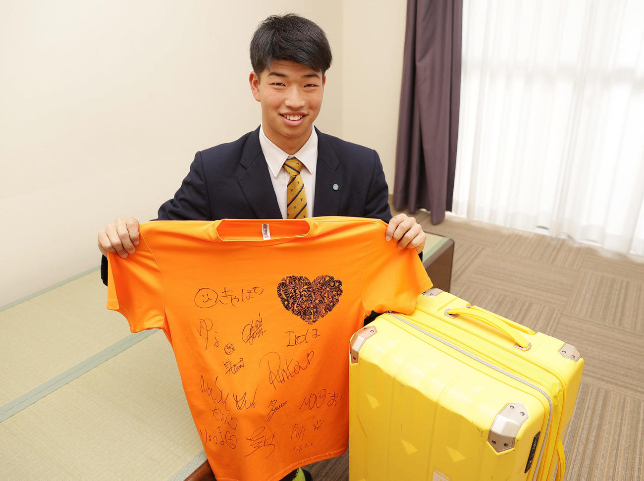 入寮し持ち込んだクラスメートのサインが書かれたTシャツを手に笑顔を見せる阪神百崎（撮影・前田充）