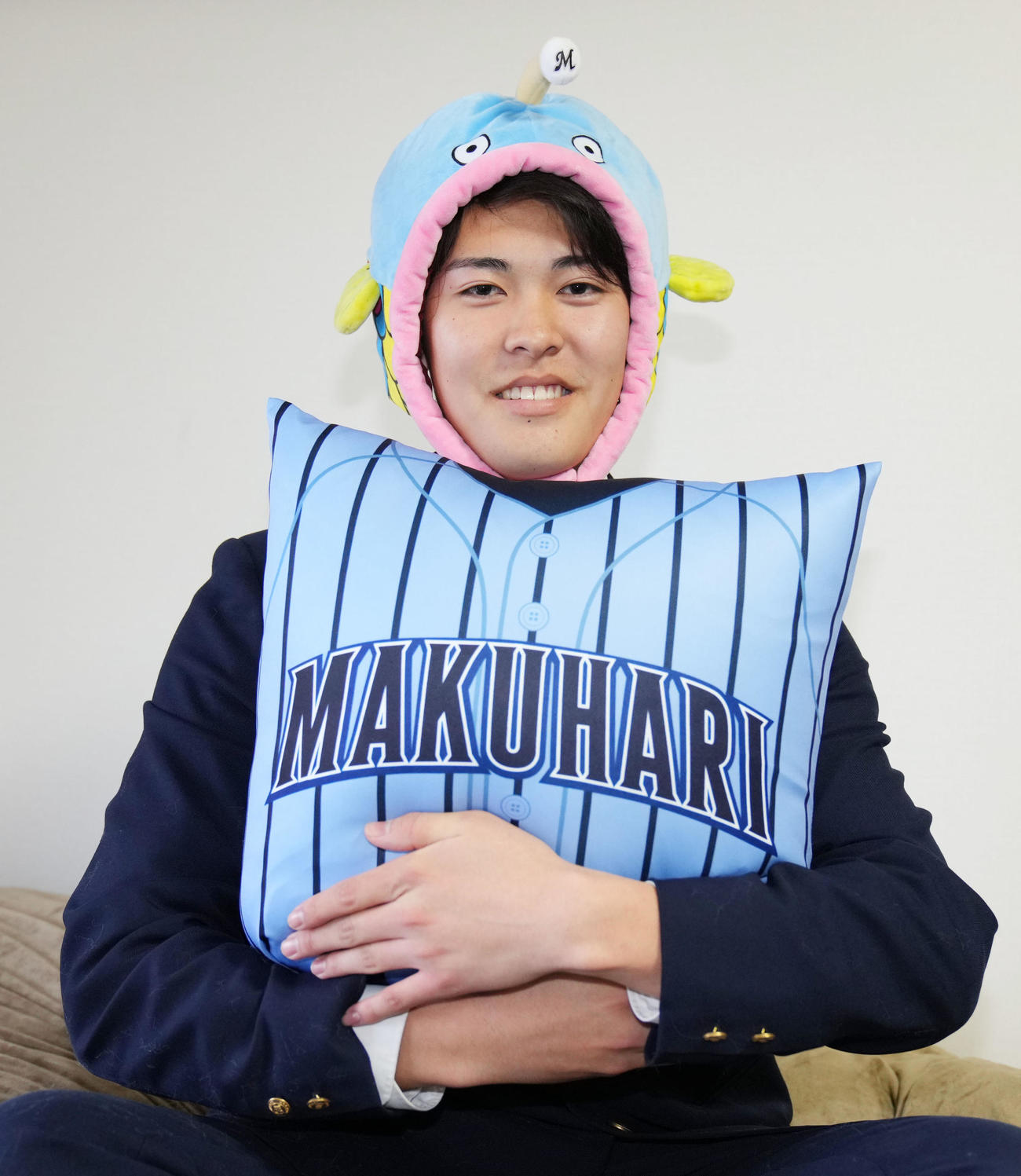 入寮の際に持参した謎の魚と友人からプレゼントされたクッションを持ち笑顔を見せるロッテドラフト4位の幕張総合・早坂（撮影・横山健太）
