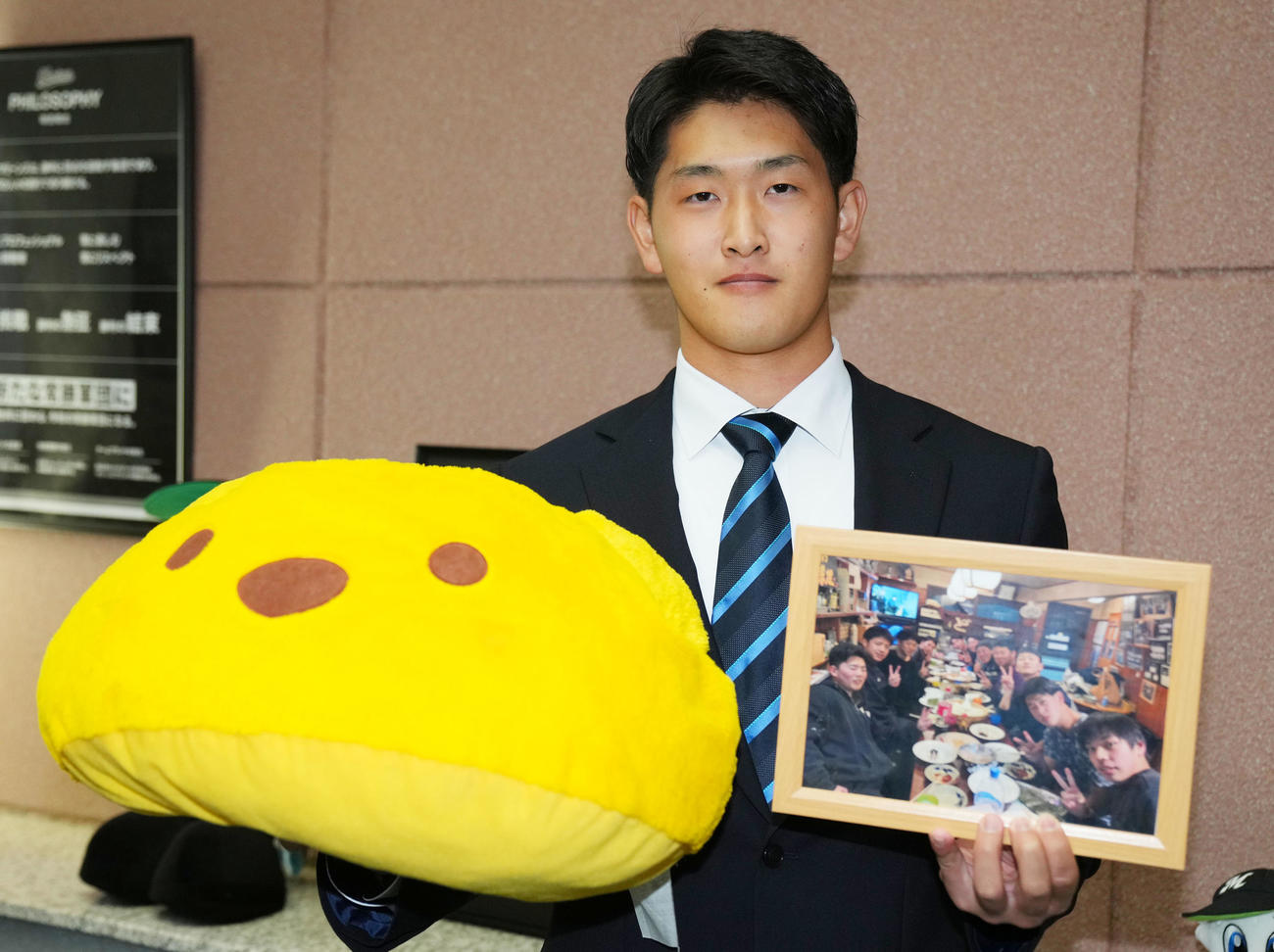 入寮に持参したプーさんぬいぐるみと写真を手に笑顔をみせるロッテドラフト育成3位のNLB富山・高野（撮影・横山健太）
