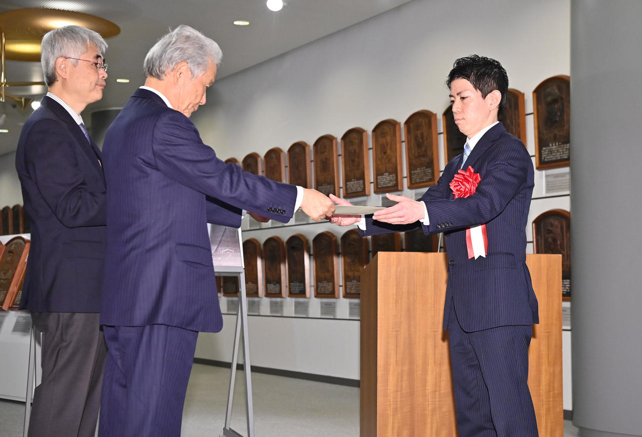 榊原コミッショナーから野球殿堂入り通知書を受け取る故・谷村友一氏の孫の米井氏（右）（代表撮影）