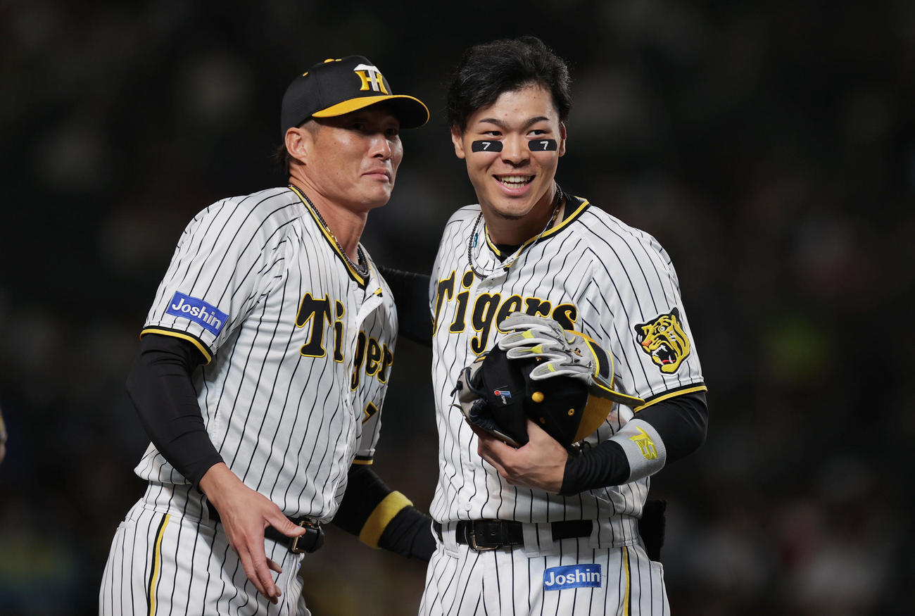 両頬に「7」を記した佐藤輝は、糸井から守備用具を受け取り笑顔を見せる（2022年9月撮影）