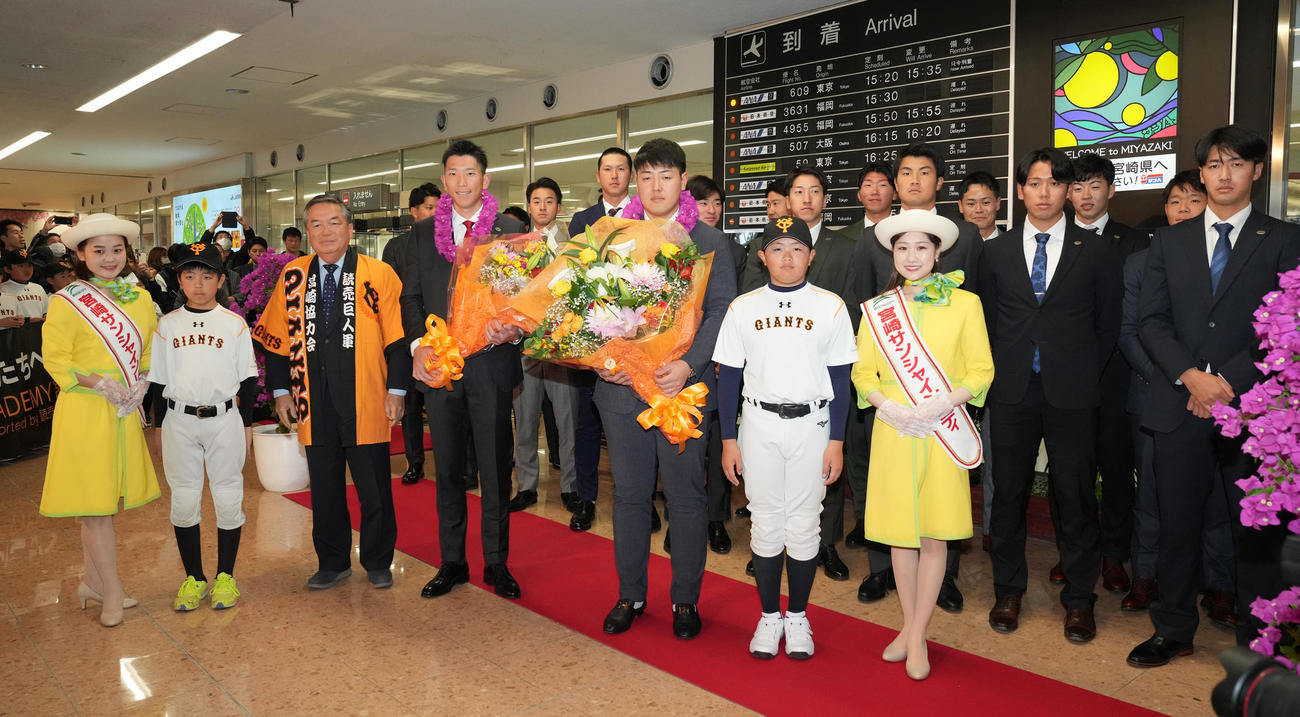 宮崎空港に到着し、歓迎セレモニーで花束を手に記念撮影する巨人岡本和（前列中央右）と戸郷（同左）。右は西舘（撮影・鈴木みどり）