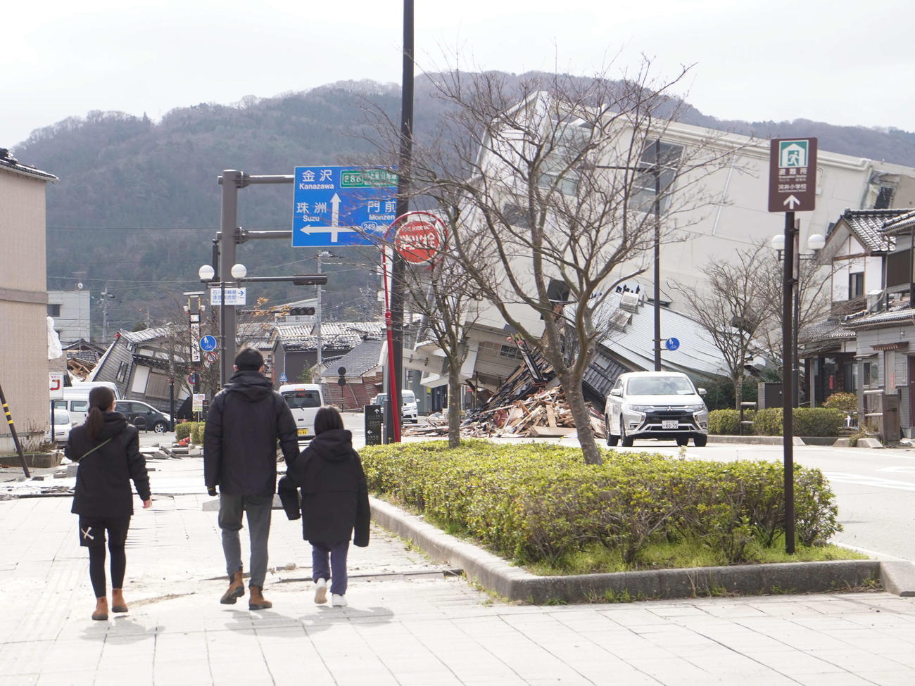 地震の影響でビルが根こそぎ倒れるなどの甚大な被害を受けた石川県輪島市内の街を歩く親子＝2024年1月19日
