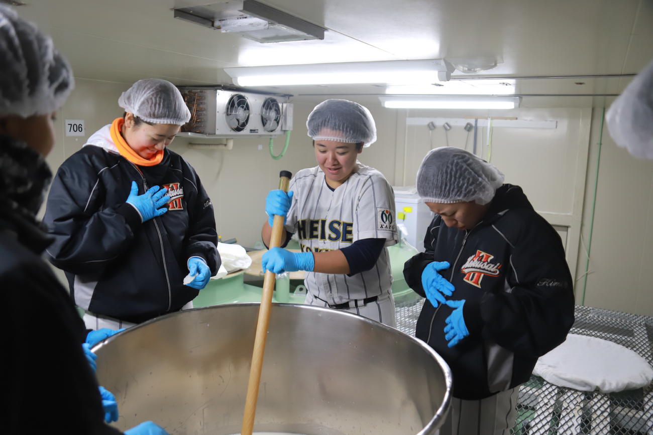 醸造タンクをかき混ぜていると液体がはねてびっくりする平成国際大女子野球部の選手たち