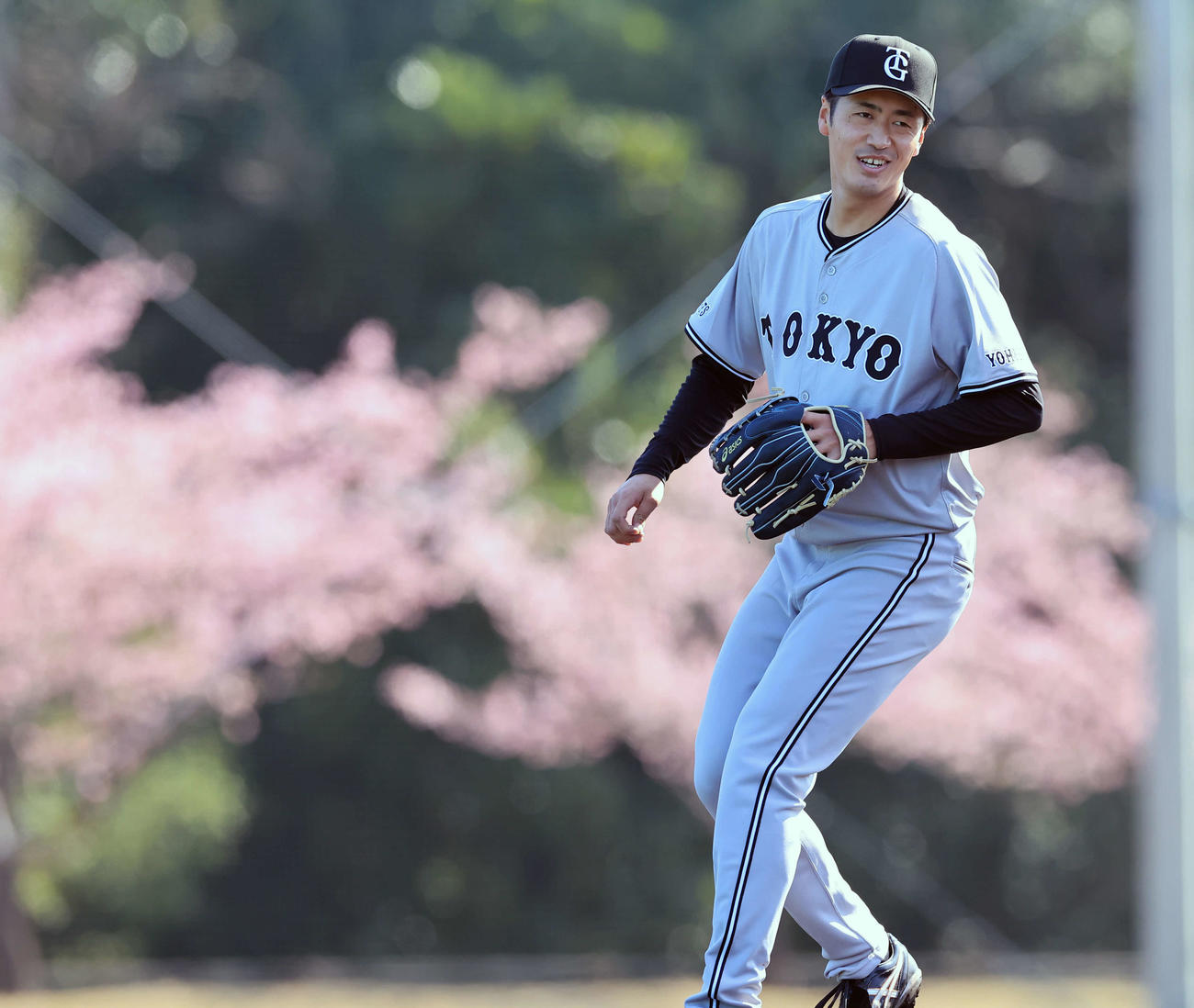満開の河津桜を背にノックを受けて笑みを浮かべる巨人西舘（撮影・浅見桂子）