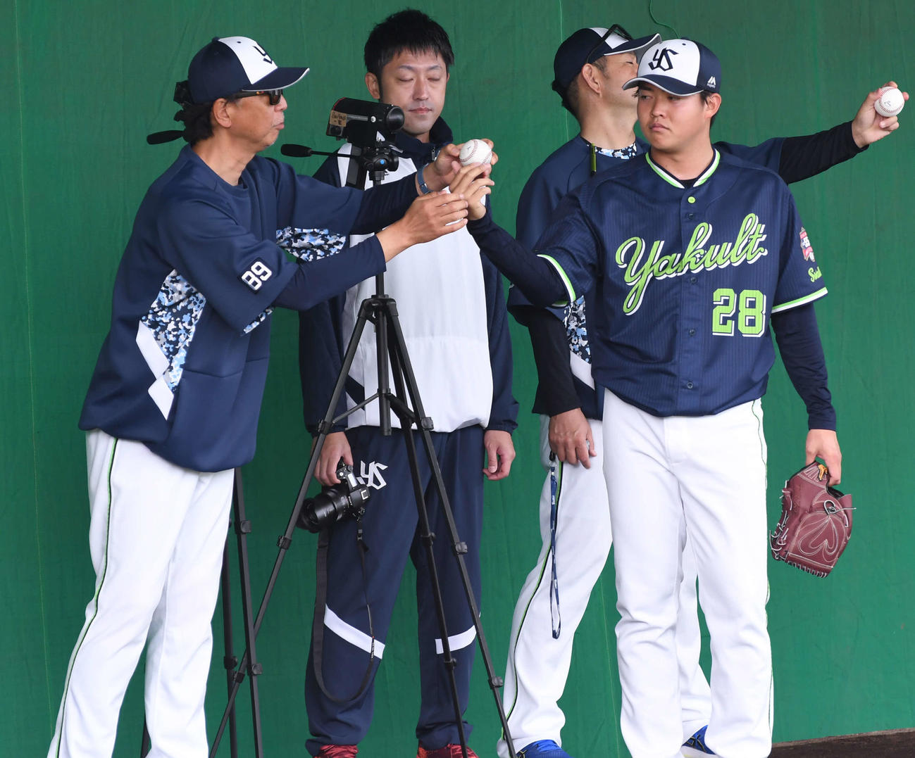 ブルペンでヤクルトのドラフト2位松本（右）にスライダーの握りを見せる伊藤投手コーチ（左）と、スライダーの握りを確認する石井投手コーチ（左から3人目）