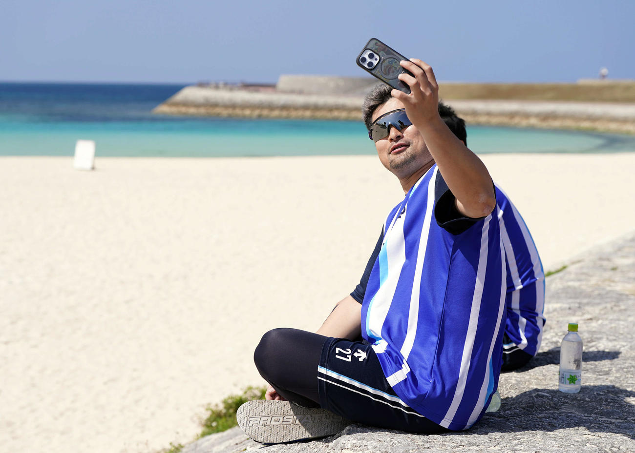携帯で海を背に自撮りをするDeNA森唯（撮影・たえ見朱実）