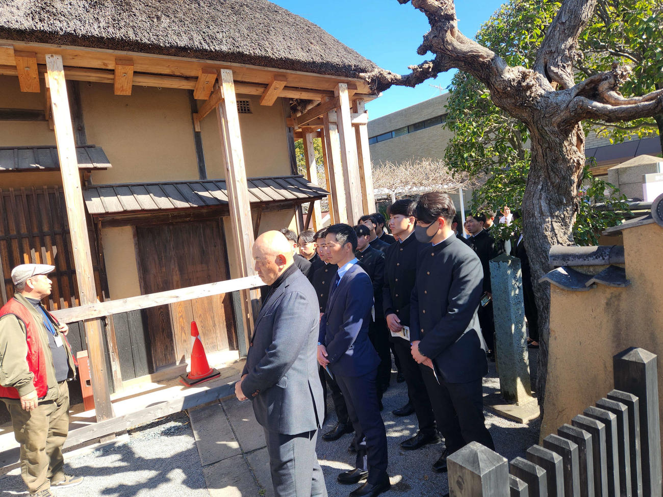 大分県の中津合宿初日。慶応の創始者である福沢諭吉の旧居を見学し、観光ガイドの説明を熱心に聞く慶大の堀井哲也監督と選手たち（撮影・保坂淑子）