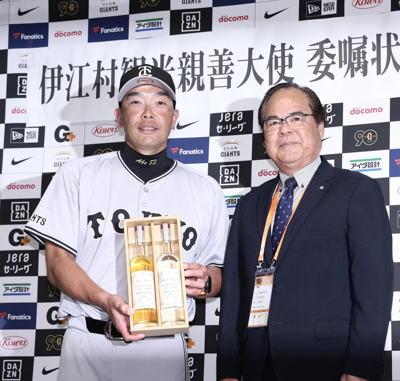 伊江村観光親善大使の巨人阿部監督（左）は、委嘱状交付式で名城村長から伊江村のラム酒を受け取る（撮影・河田真司）