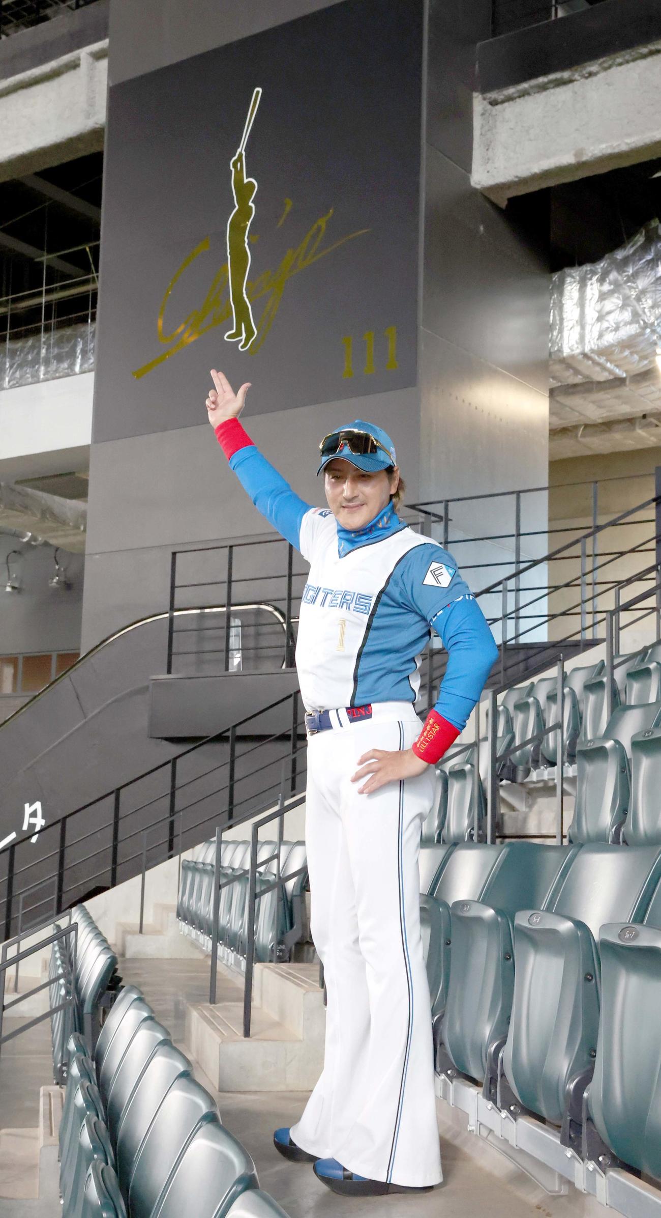 レフトスタンドに新たに設置された看板の前でポーズをとる日本ハム新庄監督（撮影・黒川智章）
