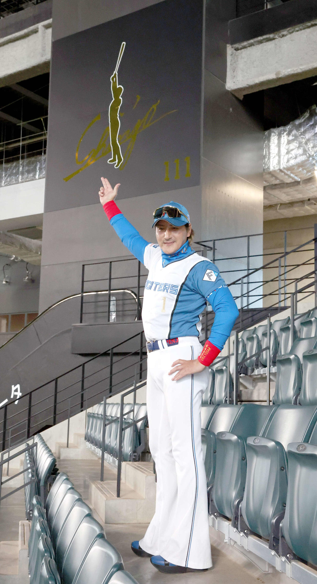 レフトスタンドに新たに設置された看板の前でポーズをとる日本ハム新庄監督（撮影・黒川智章）