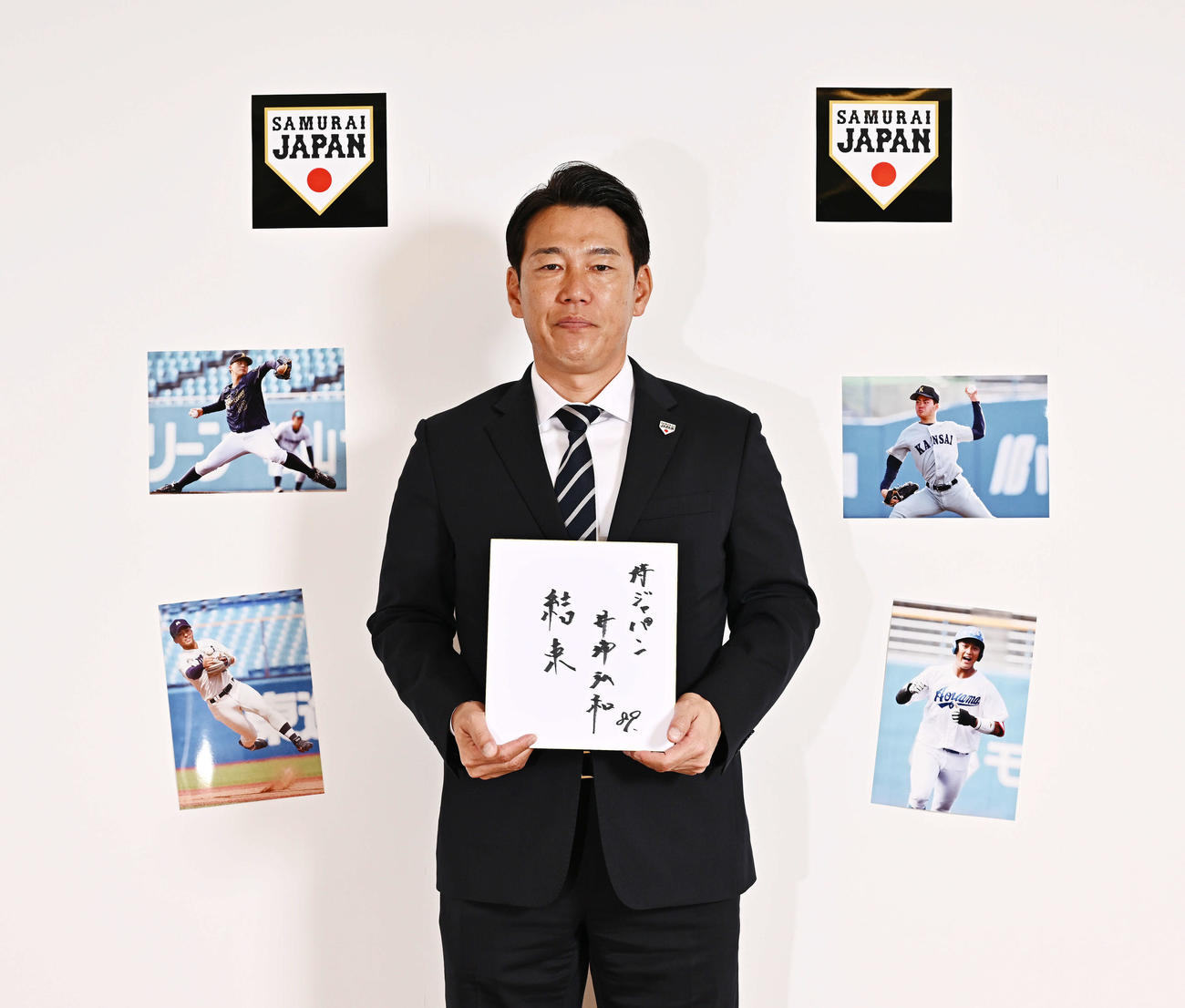 色紙に「結束」と記した侍ジャパン井端監督。壁に貼られた写真は左下から時計回りに、明大・宗山、愛知工大・中村、関大・金丸、青学大・西川（撮影・滝沢徹郎）