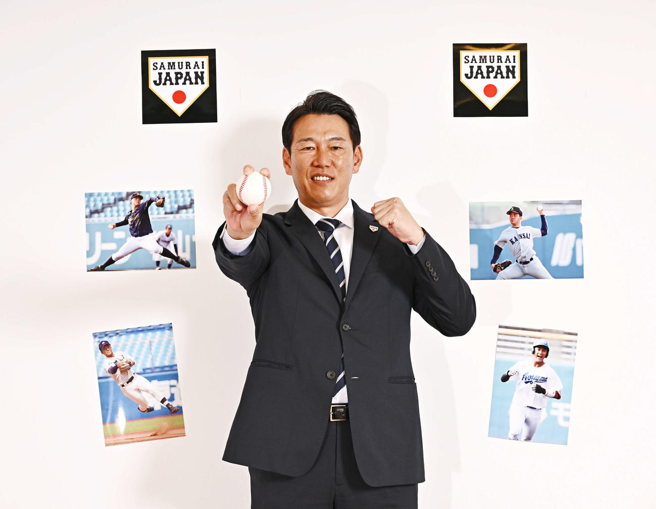ボールを手にガッツポーズする侍ジャパン井端監督。壁に貼られた写真は左下から時計回りに、明大・宗山、愛知工大・中村、関大・金丸、青学大・西川（撮影・滝沢徹郎）