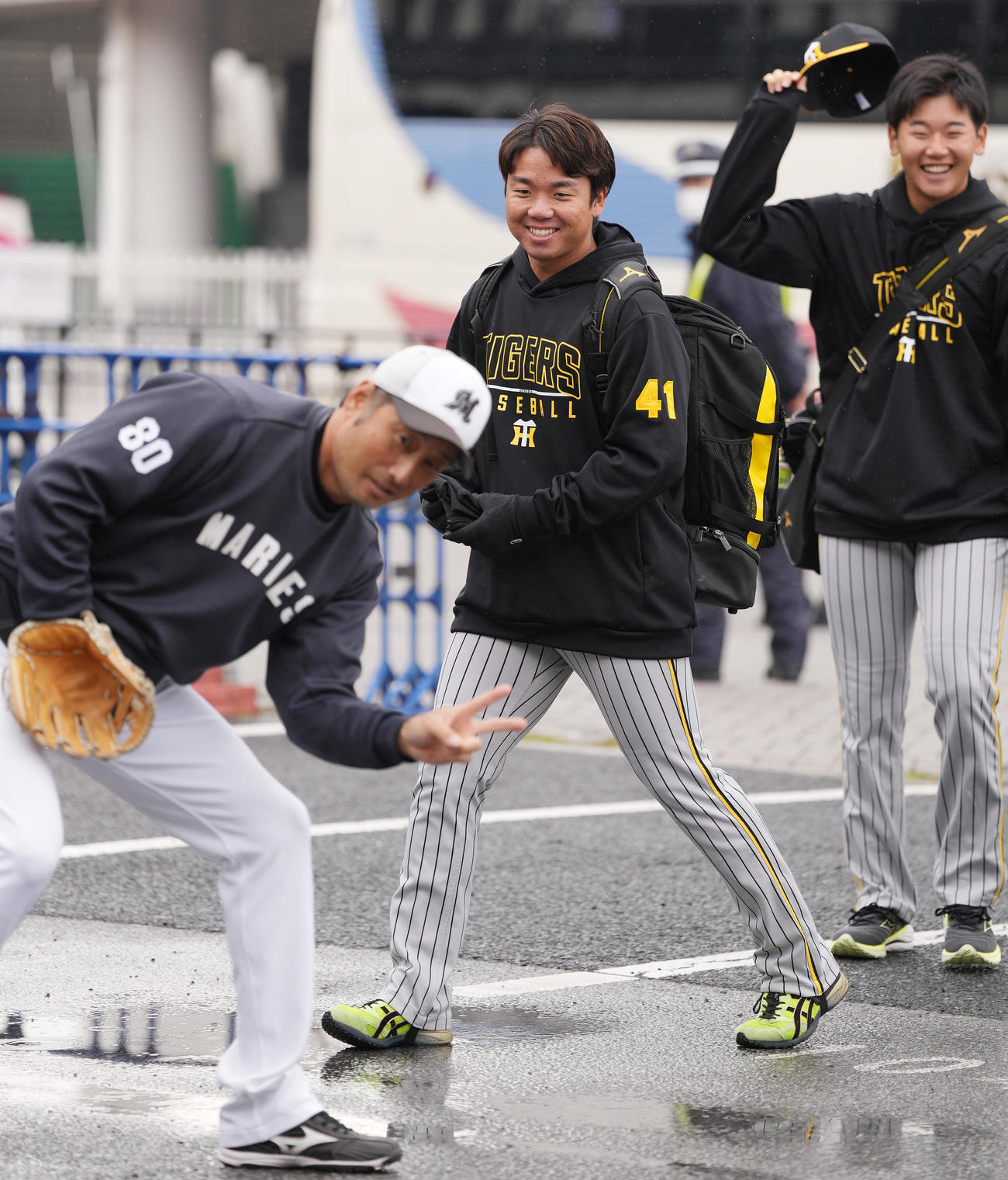 外で寝そべるカメラマンに向けピースするロッテ大塚外野守備走塁コーチ（左）を笑顔で見る阪神村上（中央）と門別（撮影・鈴木みどり）