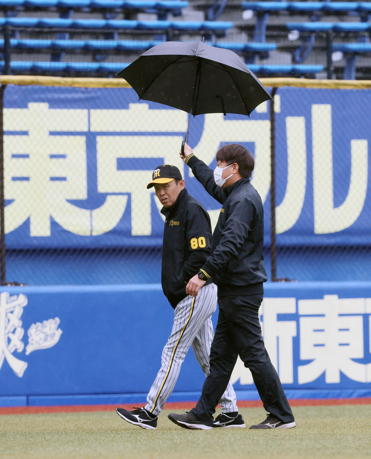 ロッテ対阪神　藤原広報（右）に傘を差して貰い外野を移動する岡田監督（撮影・加藤哉）