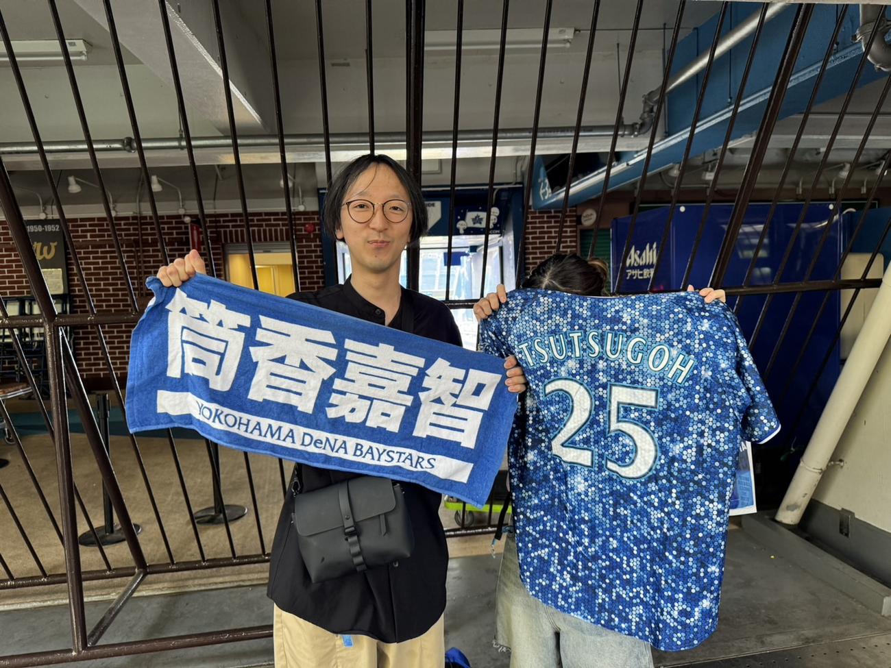 筒香のユニホームとタオルを掲げるDeNAファンの30代男性（左）と20代女性
