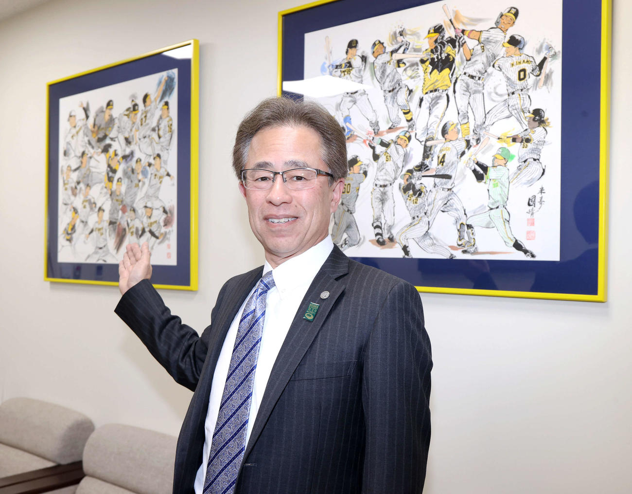 昨シーズン日本一に輝いた選手たちのイラストと写真に納まる阪神粟井球団社長（撮影・上山淳一）