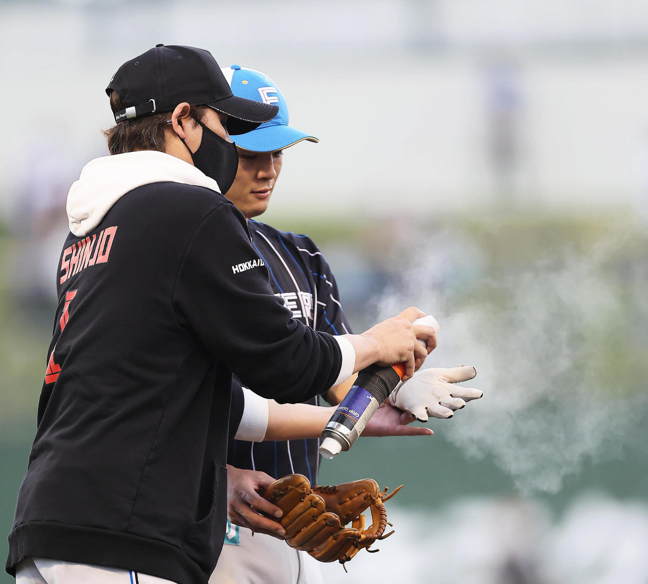 試合前の練習を行う日本ハム郡司（右）の手袋にスプレーをかける新庄監督（撮影・足立雅史）