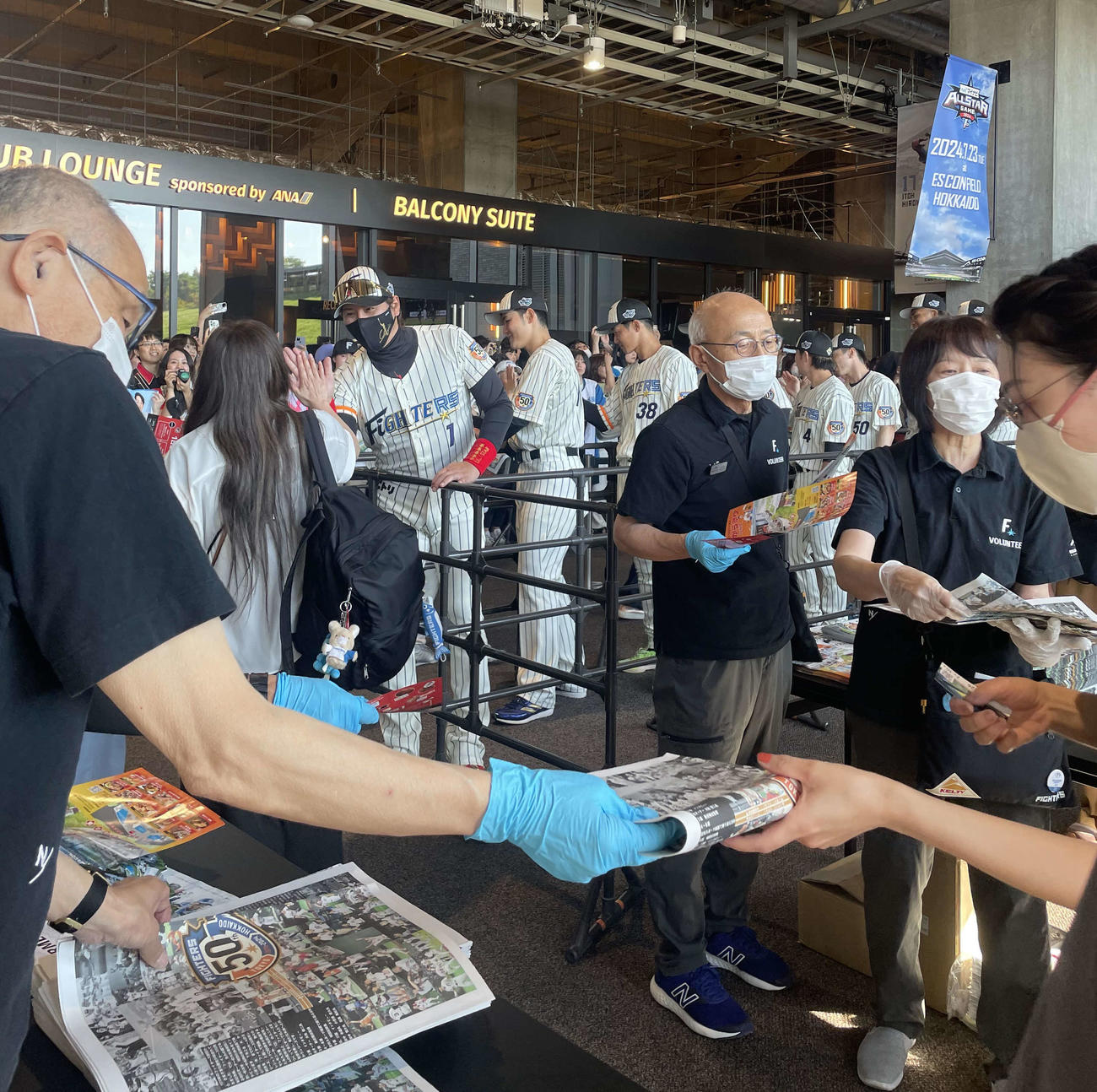 ファンとハイタッチをする日本ハム新庄監督（左から3人目）と来場者に配布された「ファイターズ50周年記念紙」（手前）