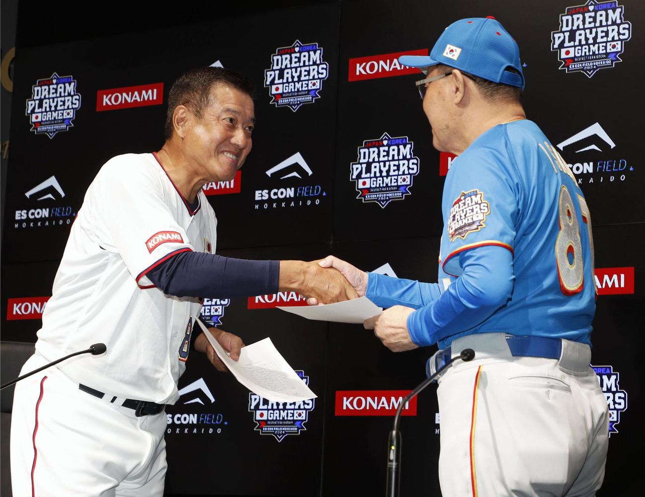 試合前の記者会見を終え、メンバー表を交換し握手を交わす日本の原辰徳監督（左）と韓国の金寅植監督（共同）