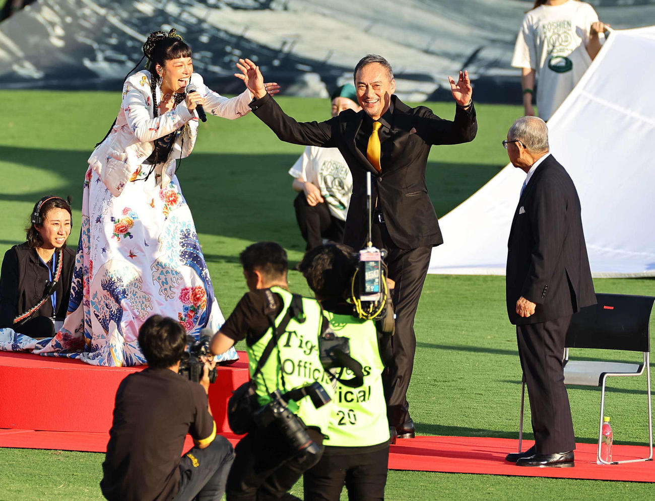 2024年8月1日、阪神対巨人　甲子園100周年のステージで歌うAI（左）と笑顔を見せる渡辺謙