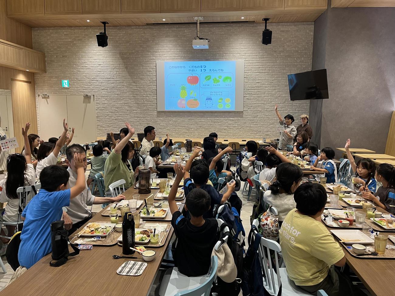 球団職員の食堂で食事をしながらスタッフのクイズにこたえる児童たち