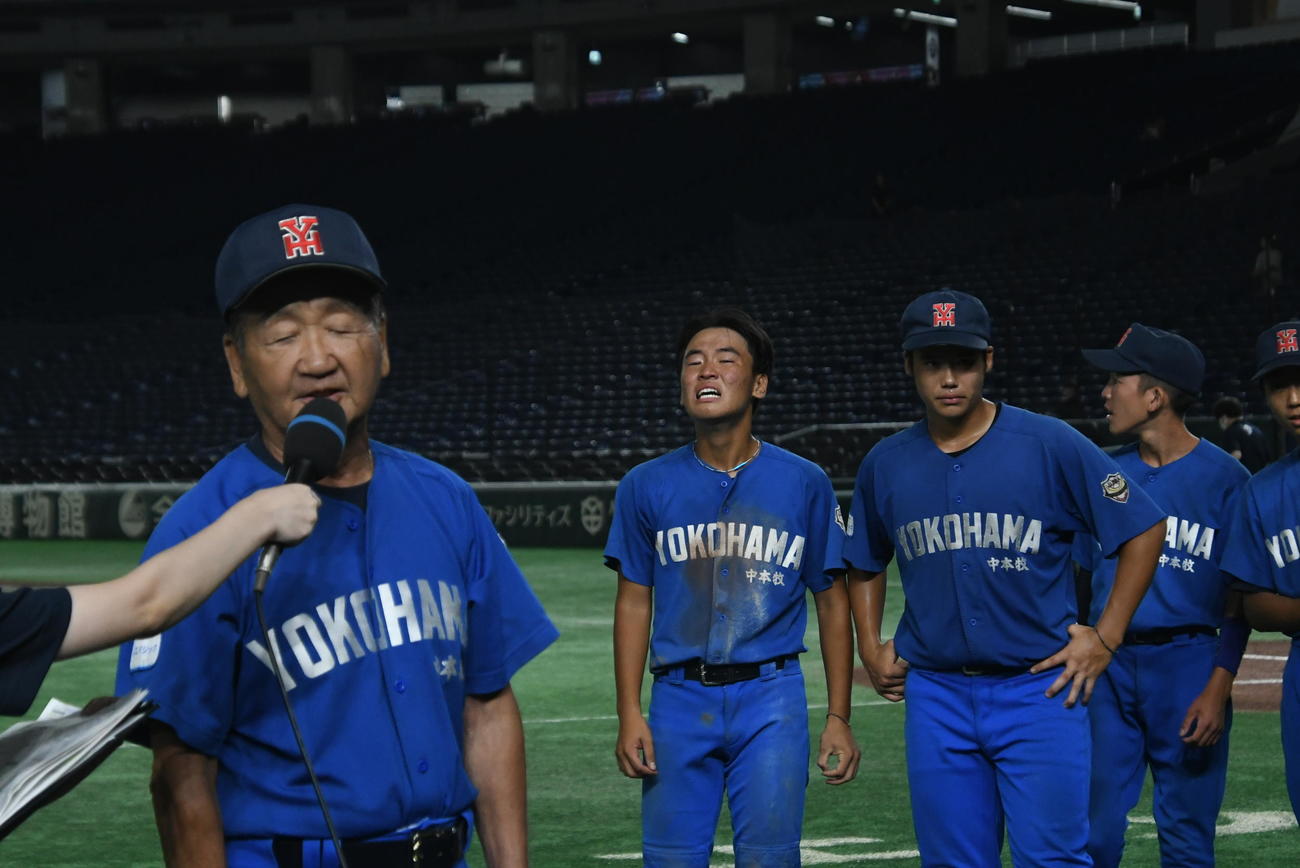優勝インタビューを受ける76歳の村上監督の向こうで、泣きじゃくる捕手の陶山。正捕手の北垣が負傷して不在の中、左腕コンビをていねいにリードしてきたのが報われた（写真・久我悟）
