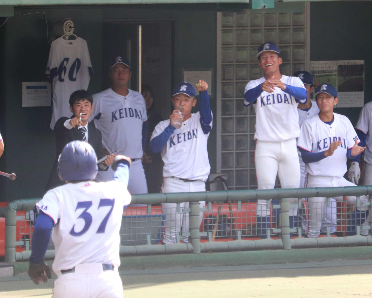 大商大との1回戦　3回無死一、二塁で大経大の柴崎が右越え適時打を放つと、下山がガッツポーズで生還。ベンチでは、高代監督のユニホームが飾られている。