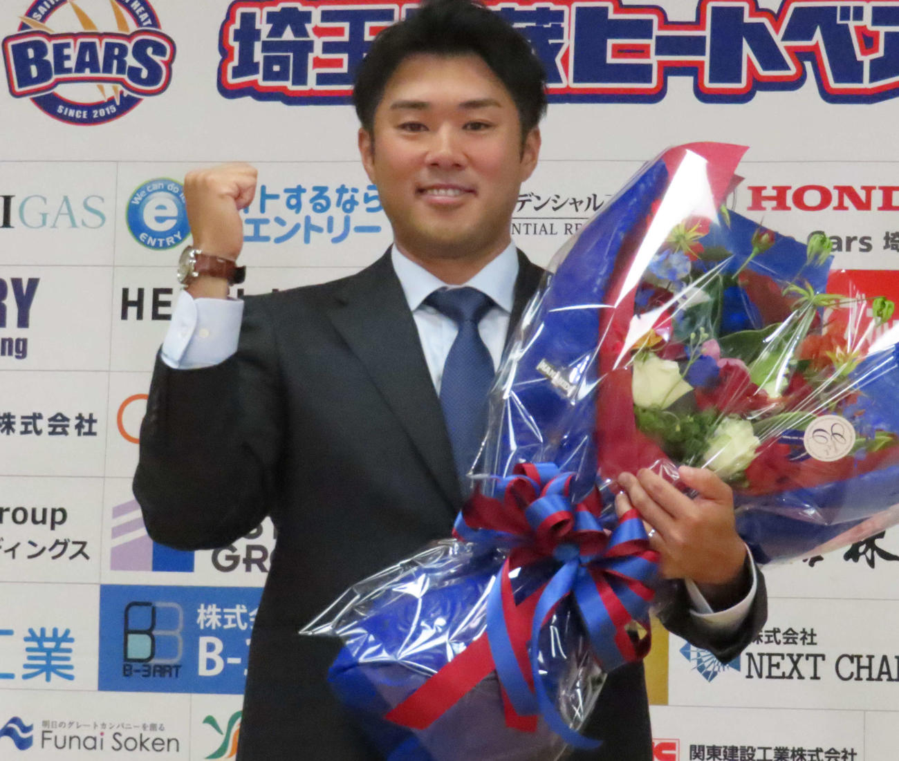 引退会見に臨み、花束を手にガッツポーズするBC埼玉・由規（撮影・水谷京裕）