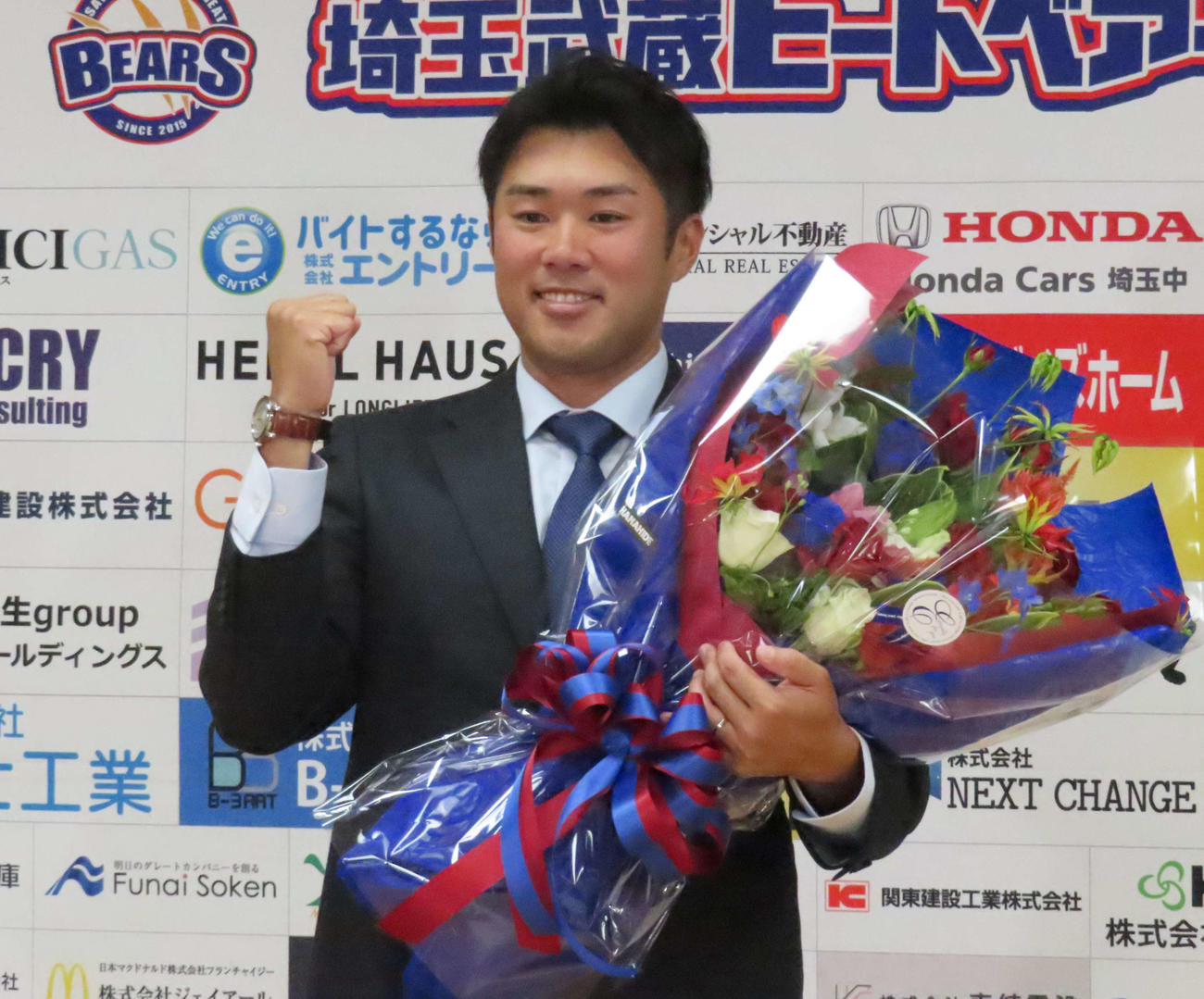 引退会見に臨み、花束を手にガッツポーズするBC埼玉・由規（撮影・水谷京裕）