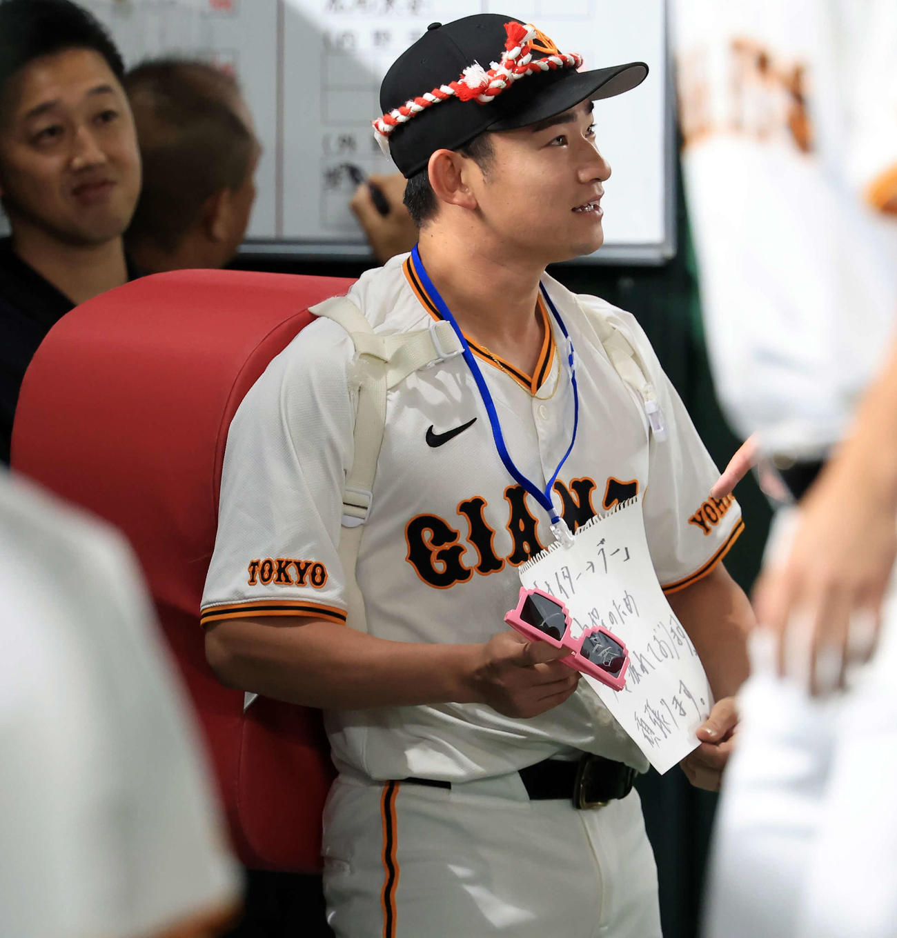 巨人対DeNA　巨人の試合前円陣の声出しに登場した赤いカバン？を背負った萩尾のボードには「ナイター→デー日程のため少々疲れております」と書かれていた（撮影・浅見桂子）