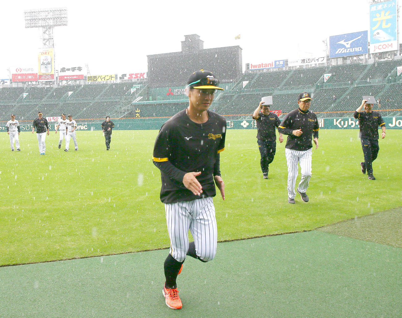 雨が降りグラウンドから避難する阪神熊谷（手前）、平田2軍監督ら（撮影・上山淳一）