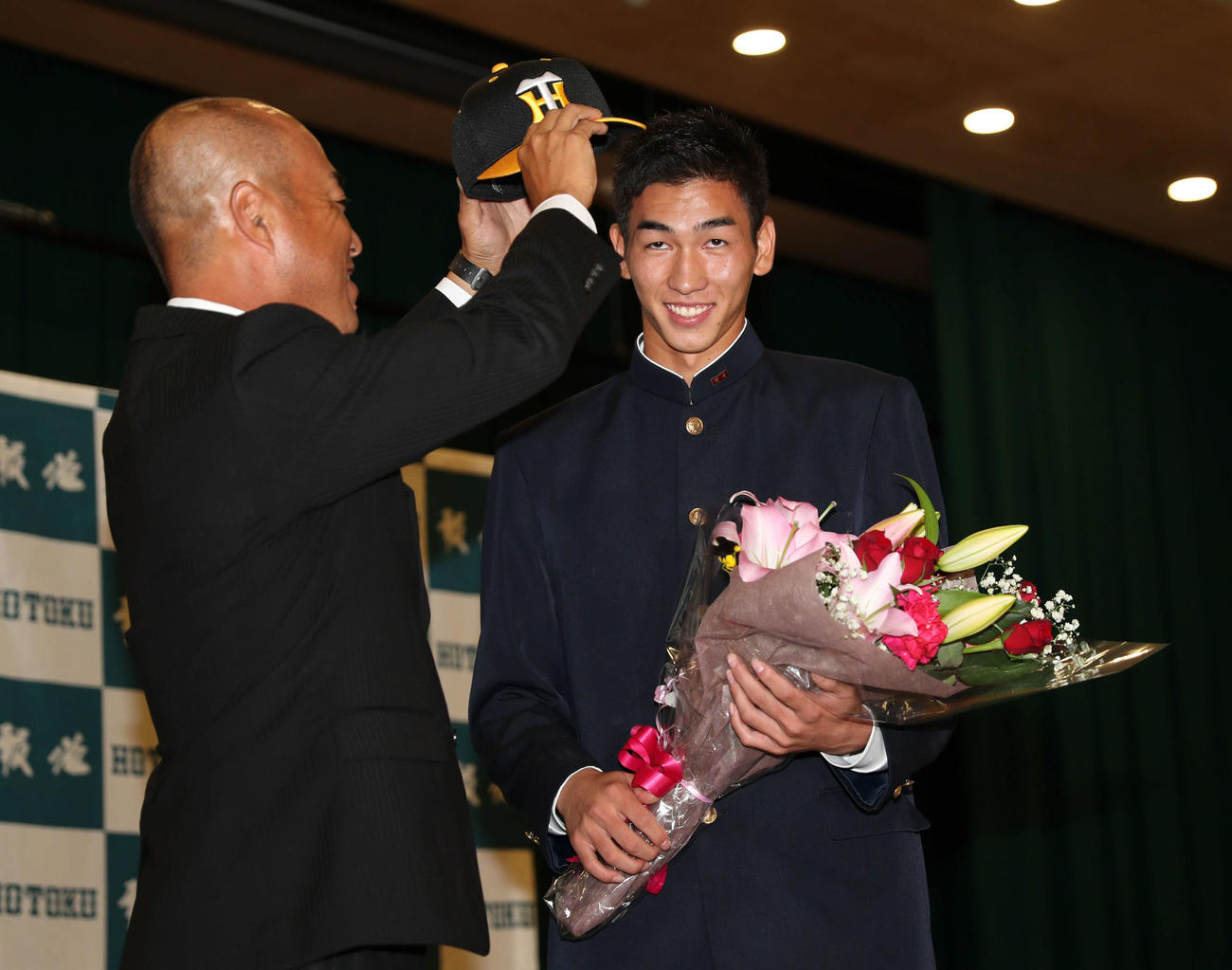 阪神2位指名の報徳学園・今朝丸（右）は大角監督から阪神の帽子をかぶせてもらい笑顔（撮影・西尾就之）