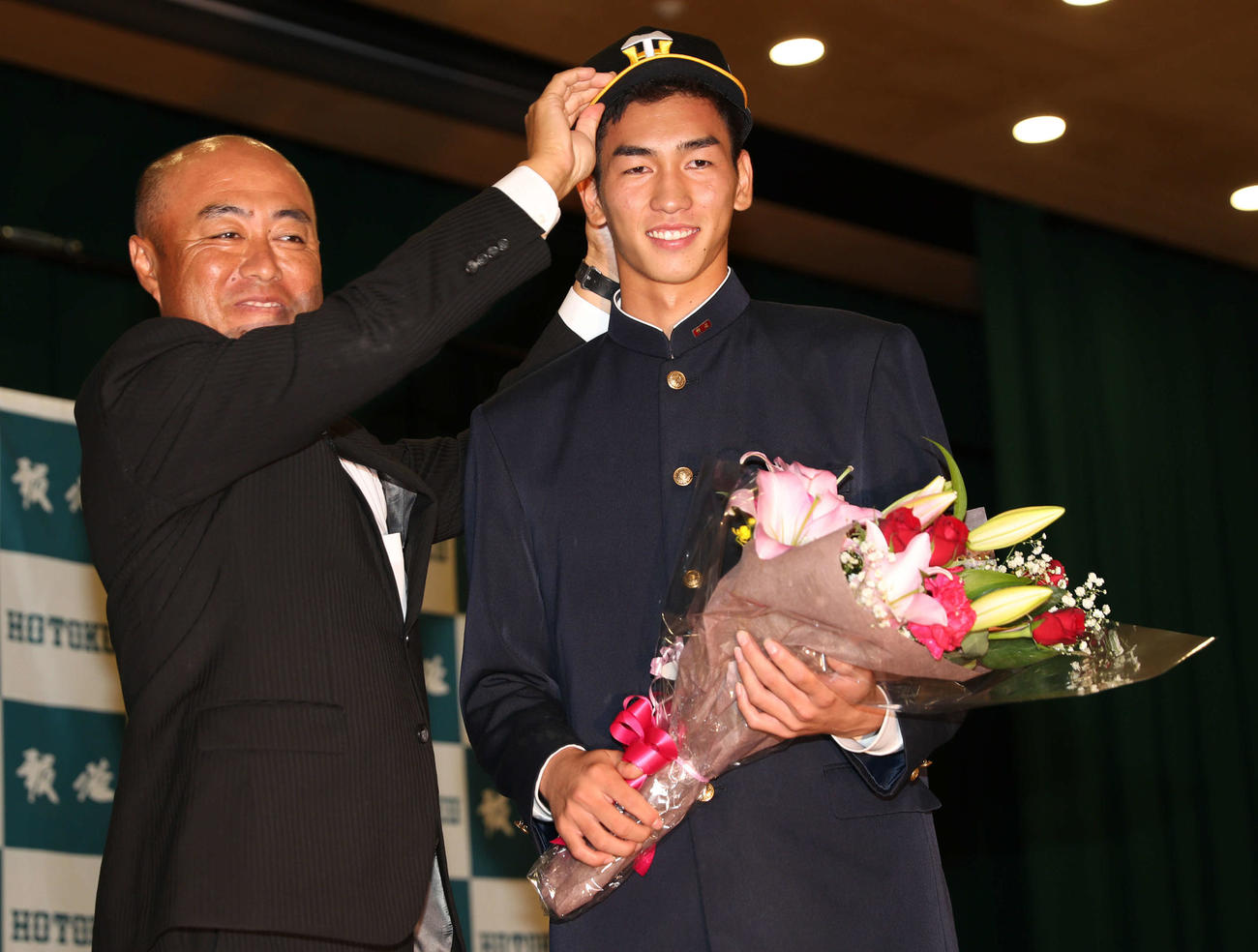 阪神2位指名の報徳学園・今朝丸（右）は大角監督から阪神の帽子をかぶせてもらい笑顔（撮影・西尾就之）