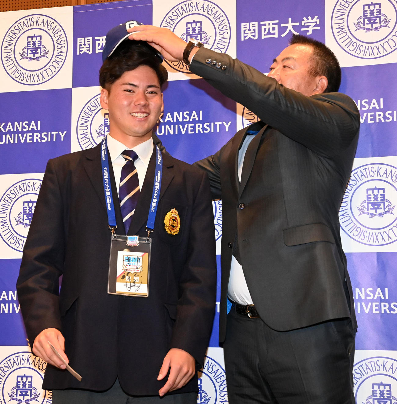 井上監督（右）から中日の帽子をかぶしてもらい笑顔を見せる関大・金丸（撮影・前岡正明）