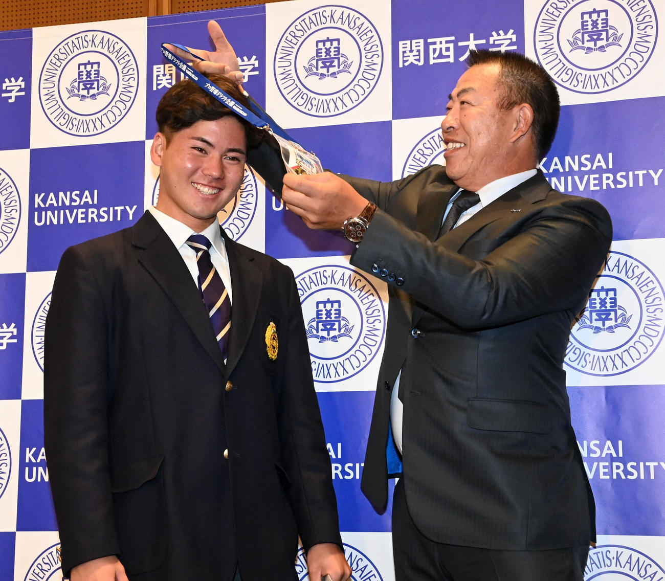 中日井上監督（右）からドラフト会場の入場パスを首にかけてもらう関大・金丸（撮影・前岡正明）