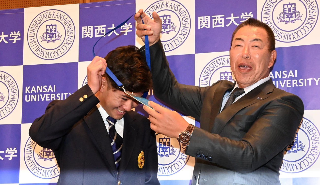 関大・金丸（左）にプレゼントするドラフト会場の入場パスを反対にかけた事に気づきやり直す中日井上監督（撮影・前岡正明）