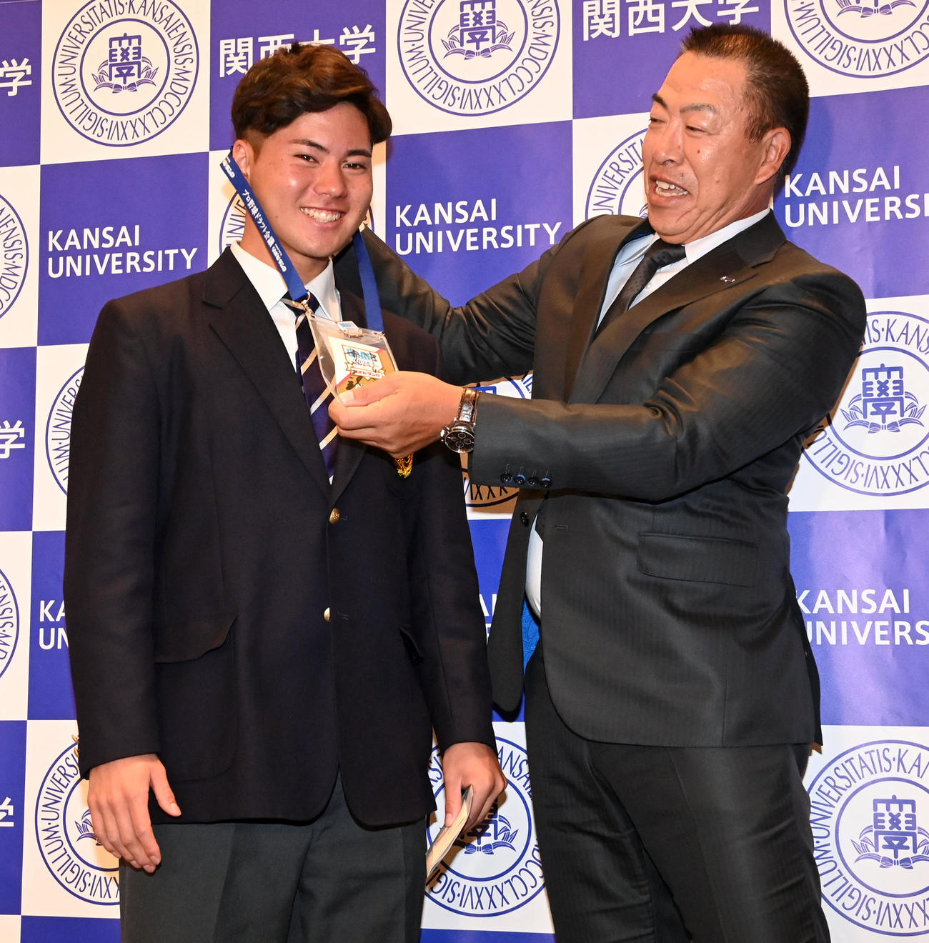中日井上監督（右）からドラフト会場の入場パスを首にかけてもらう関大・金丸（撮影・前岡正明）