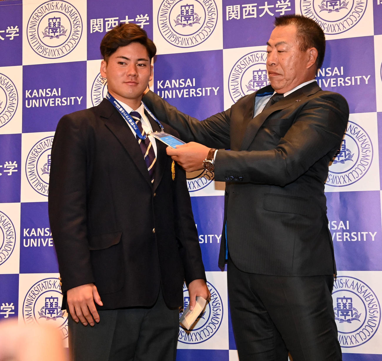 関大・金丸（左）にプレゼントするドラフト会場の入場パスを反対にかけた中日井上監督（撮影・前岡正明）