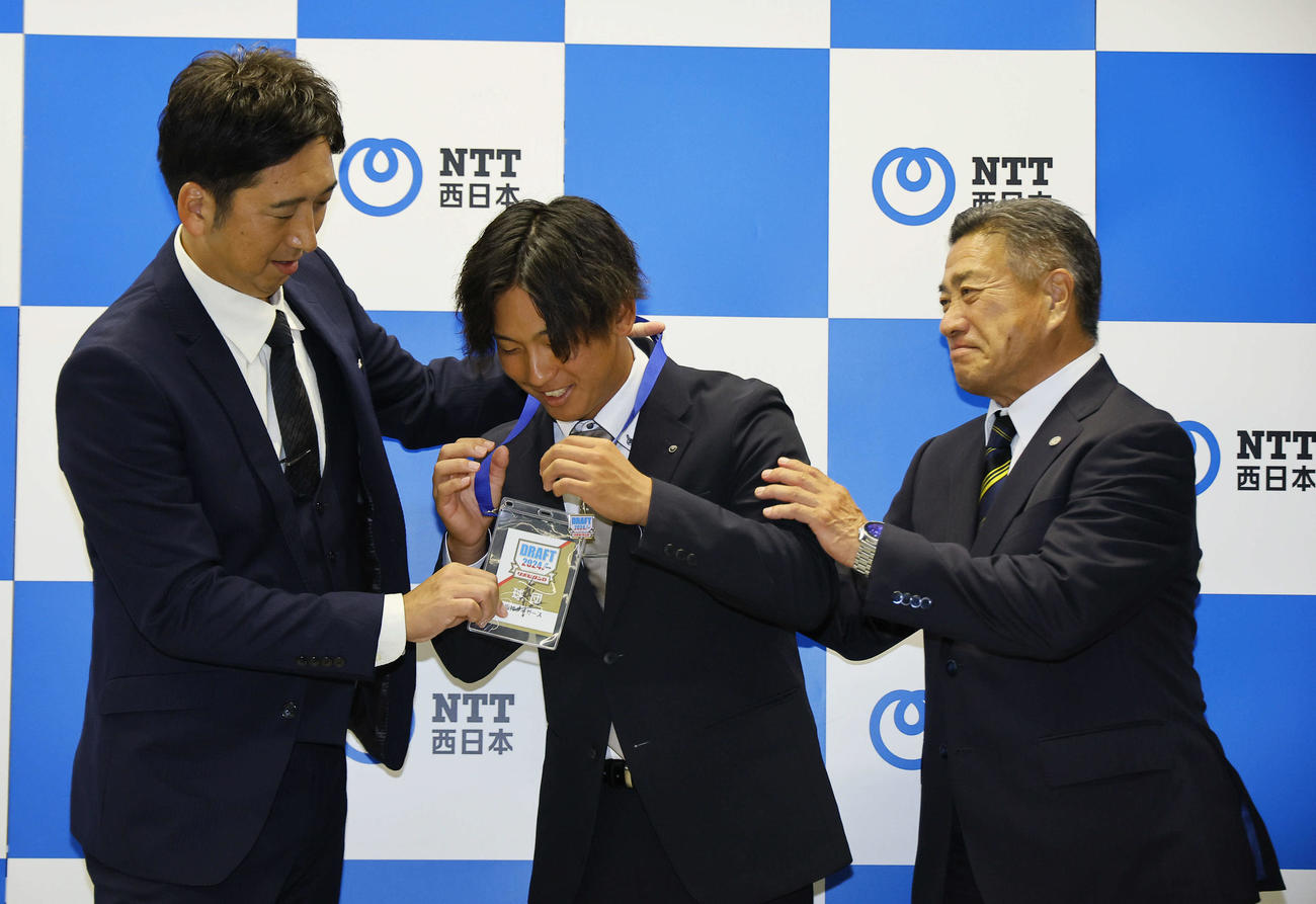 指名あいさつを終え、阪神藤川監督（左）にドラフト会議のパスを首にかけてもらうNTT西日本・伊原（中央）。右は熊野スカウト（撮影・藤尾明華）