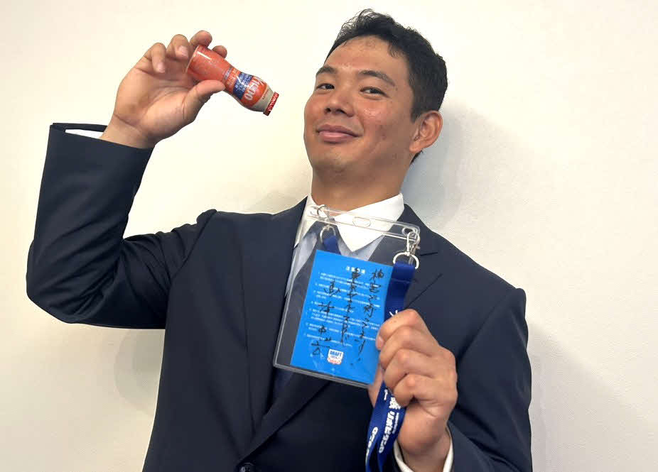 都内で指名あいさつが行われ、ドラフト会議当日の関係者パスを手にヤクルトを飲むポーズのリクエストに応えるヤクルト育成1位の根岸（撮影：佐瀬百合子）