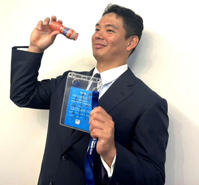 都内で指名あいさつが行われ、ドラフト会議当日の関係者パスを手にヤクルトを飲むポーズのリクエストに応えるヤクルト育成1位の根岸（撮影：佐瀬百合子）