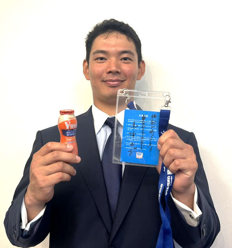 都内で指名あいさつが行われ、ドラフト会議当日の関係者パスとヤクルトを両手に笑顔を見せるヤクルト育成1位の根岸（撮影：佐瀬百合子）