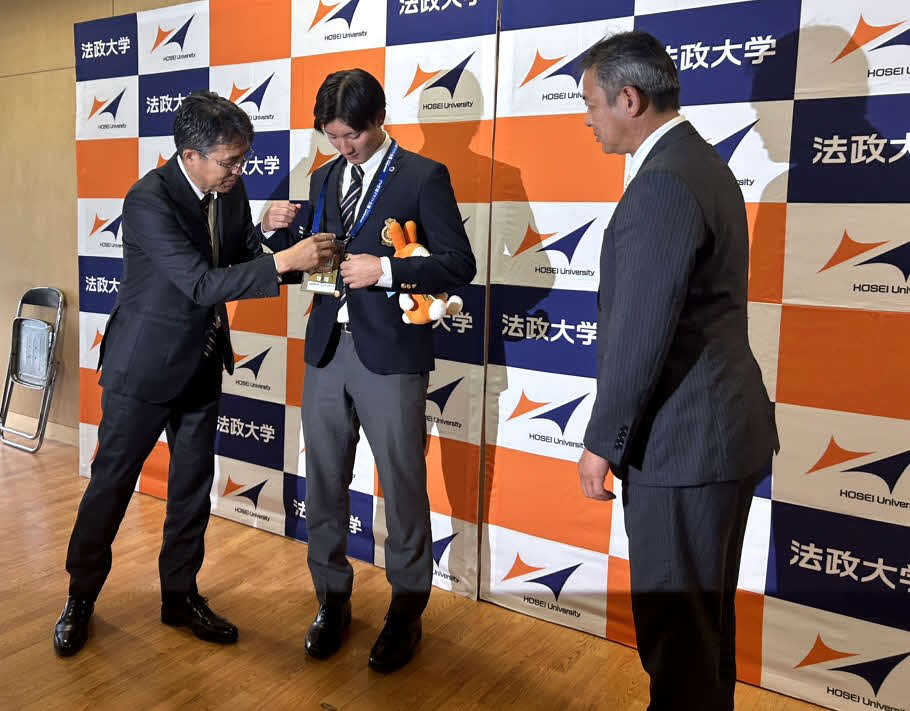 日本ハム6位指名のあいさつを受け、大渕GM補佐兼スカウト部長（左）からドラフト会議当日のパスを首にかけてもらう法大・山城（中央）。見つめる高橋スカウト（右）（撮影・佐瀬百合子）