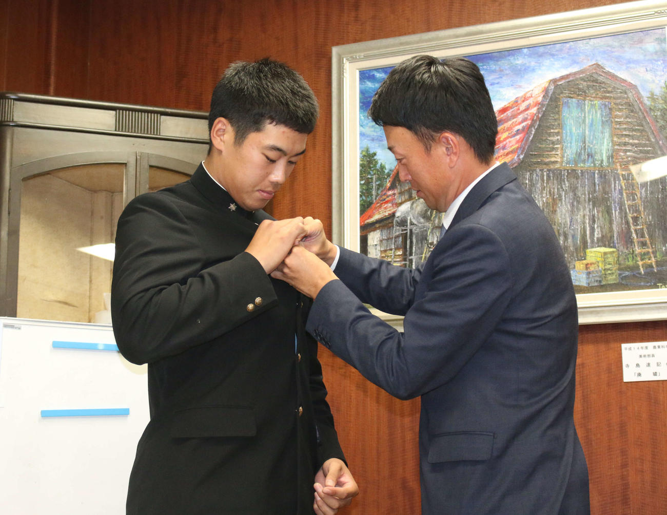 日本ハムから指名あいさつを受けた育成2位の帯広農・渋谷は取材対応中に学生服の第2ボタンが外れて西川監督（右）に付け直してもらう（撮影・木下大輔）