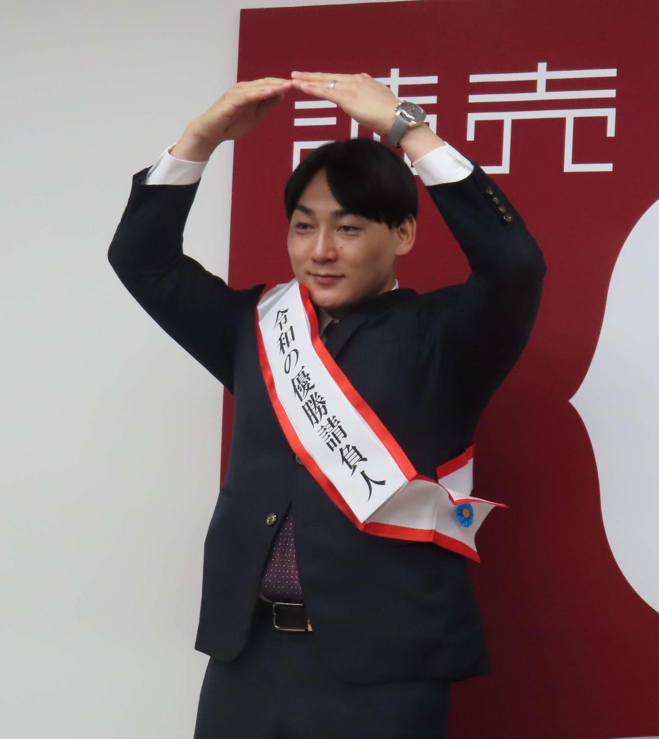 契約更改後の会見で「令和の優勝請負人」と書かれたたすきをさげ、丸ポーズを披露する巨人丸（撮影・水谷京裕）