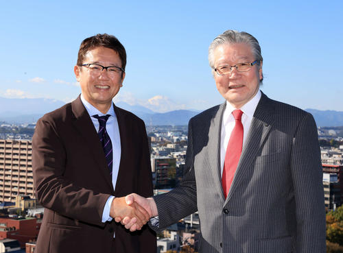 立川「SORANO HOTEL」で、山並みを背に握手する立飛の村山正道社長（右）と古田敦也理事長（撮影・浅見桂子）
