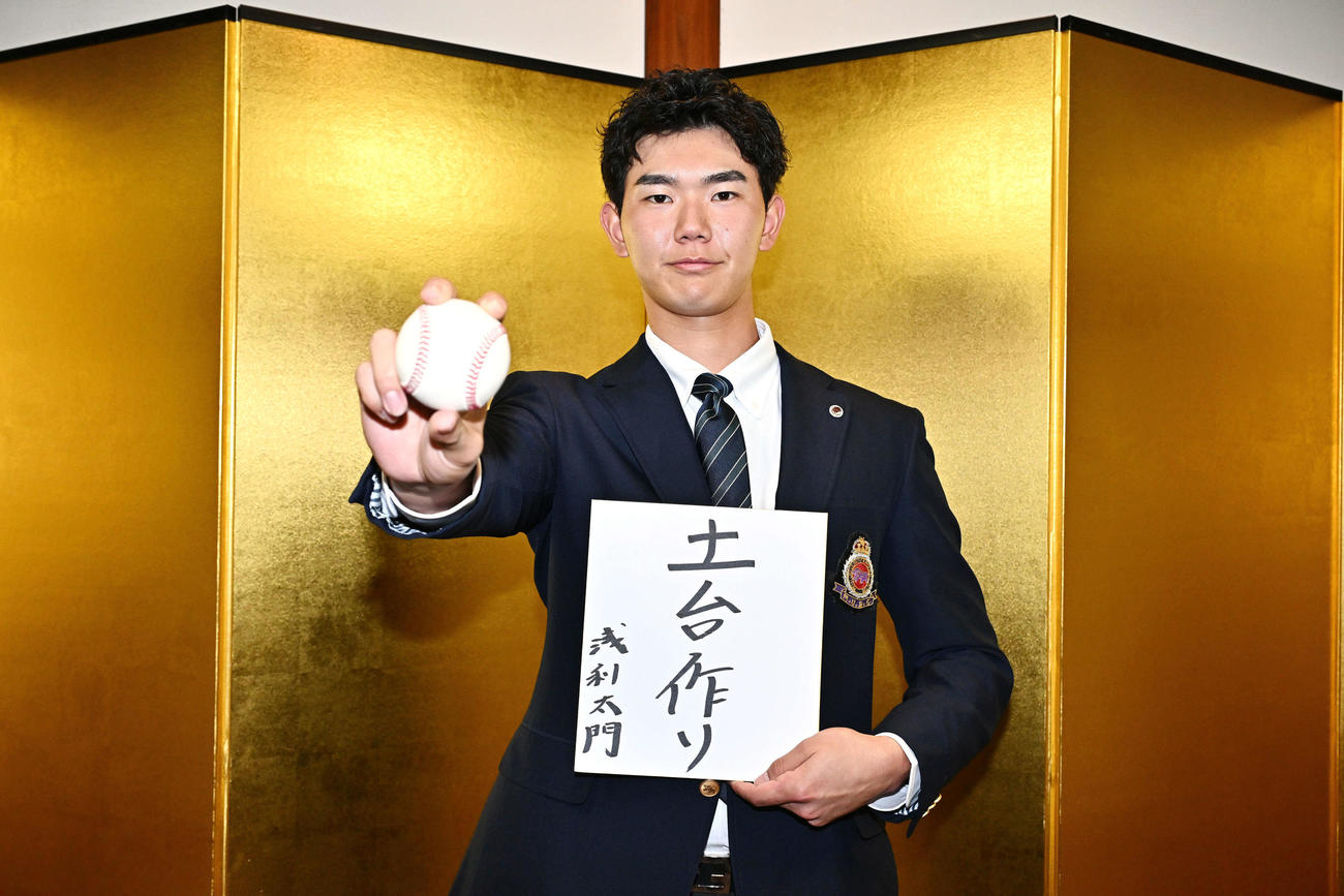 日本ハムドラフト3位の明大・浅利は金びょうぶの前で「土台作り」と記した色紙とボールを手にポーズを決める（撮影・滝沢徹郎）