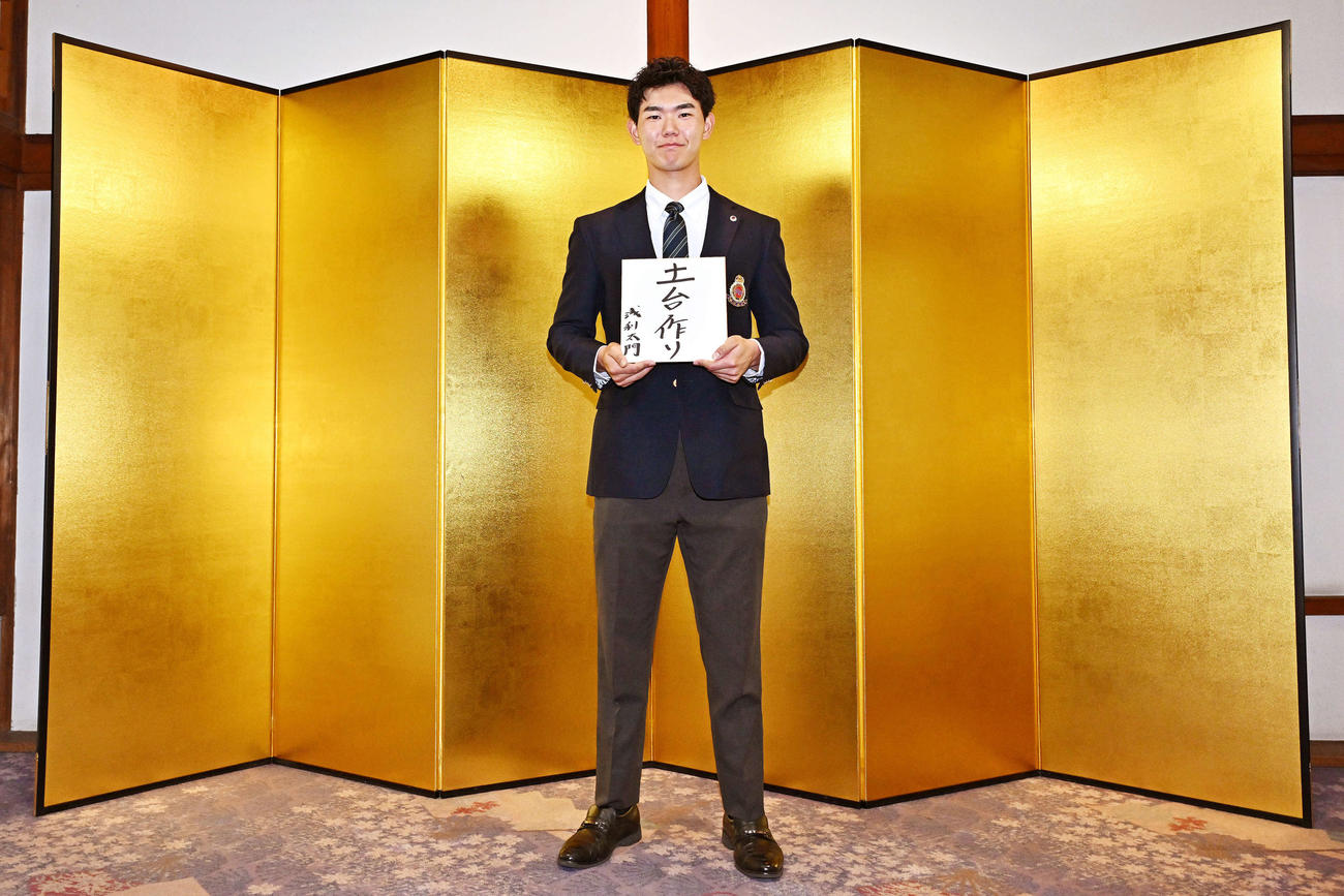 日本ハムドラフト3位の明大・浅利は金びょうぶの前で「土台作り」と記した色紙を手に写真に納まる（撮影・滝沢徹郎）